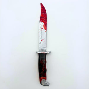 Upright, overhead view 12 inch plastic survival hunting knife inspired by the 120 Buck design from the Scream horror movie franchise, featuring a silver blade and black handle, bloody knife tip and handle, designed for cosplay or display