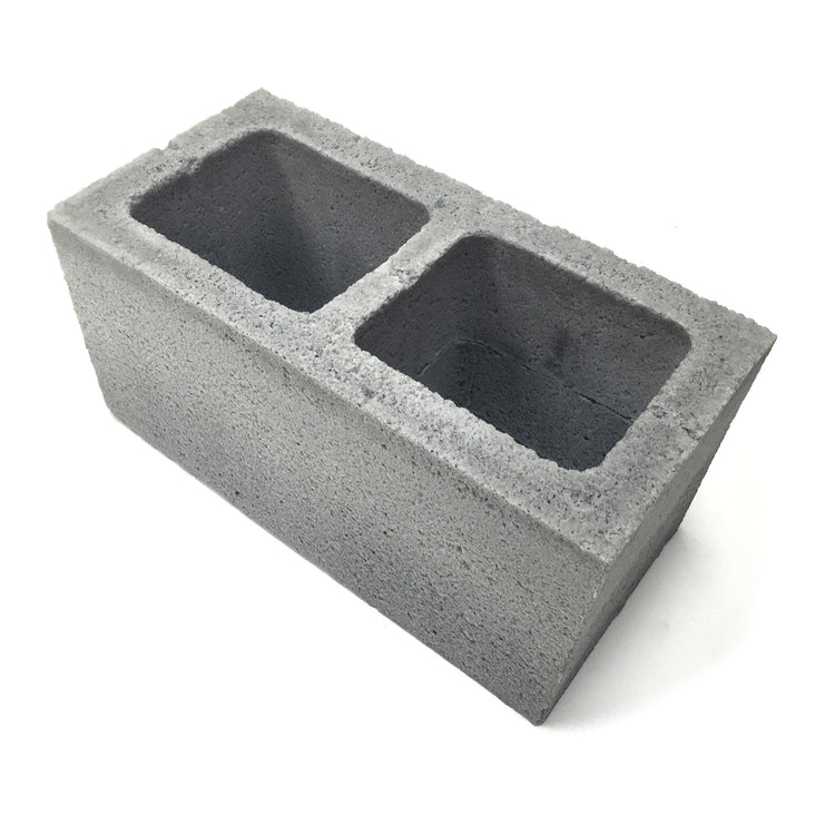 Angled view of a realistic flexible foam prop cinder block with a gray stone color and texture, designed for safe use in stunts, theater, or film