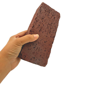 A hand holding a rectangular reddish-brown porous sponge block against a plain white background.