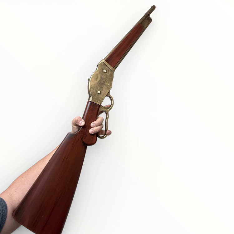Hand holding a wooden rifle with brass accents against a white background