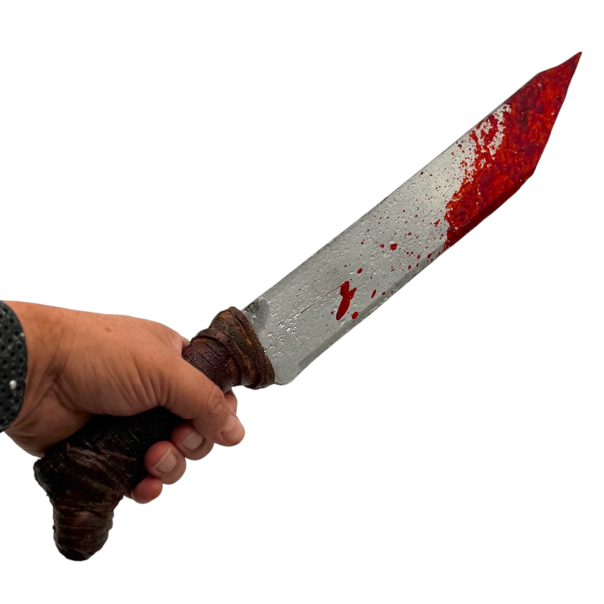 A hand holding a prop bloody knife with a silver blade covered in fake red blood splatters and a dark brown textured handle, isolated on a white background.