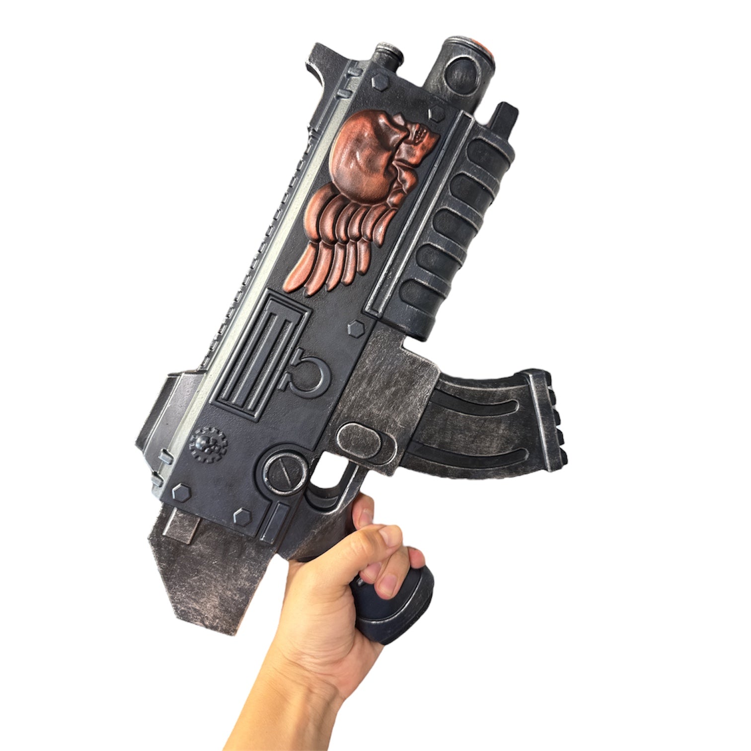 Foam Space Marine Bolter Prop Gun held in hand, featuring sci-fi design with black weathering, panel lines, curved magazine, and red-bronze skull emblem, suited for film props.