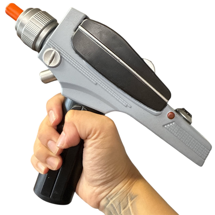 Hand holds Star Trek Phaser toy, featuring a grey and black sci-fi design with orange safety tip, trigger handle, and futuristic details.