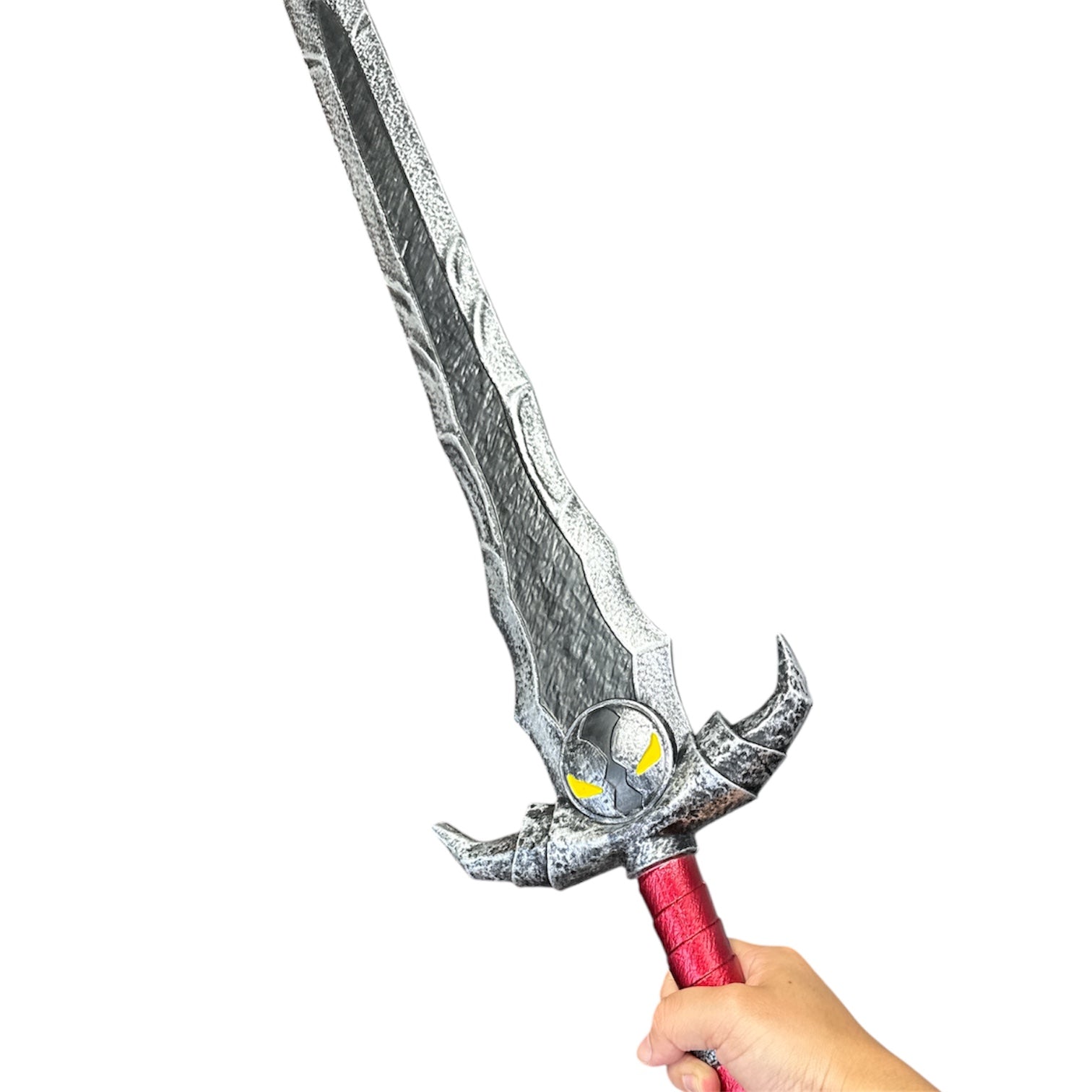 A hand grips the Foam Spawn Sword Prop, featuring a metallic-silver jagged blade, circular emblem with eye-shaped markings, and red-wrapped handle, ideal for fantasy-themed productions.