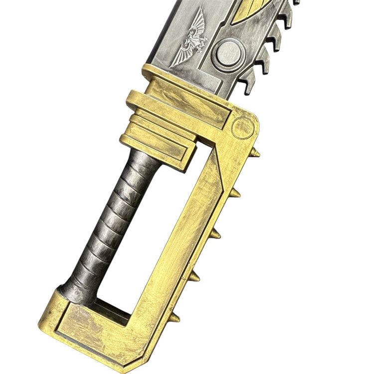 Foam Hell’s Teeth Chainsaw Prop: Close-up of brass-painted hilt with spiked grip and serrated silver blade, featuring an embossed two-headed eagle emblem.