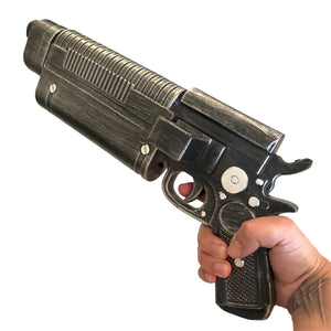 Hand holding Foam Rubber K-16 Bryar Blaster Gun Prop, a 17” x 7” x 4” steampunk-style, non-functional prop pistol designed for special effects use.