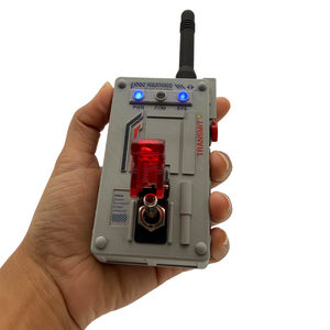 A hand holding a gray electronic transmitter device with a black antenna, blue indicator lights, a red translucent switch, and printed technical labels on a white background.