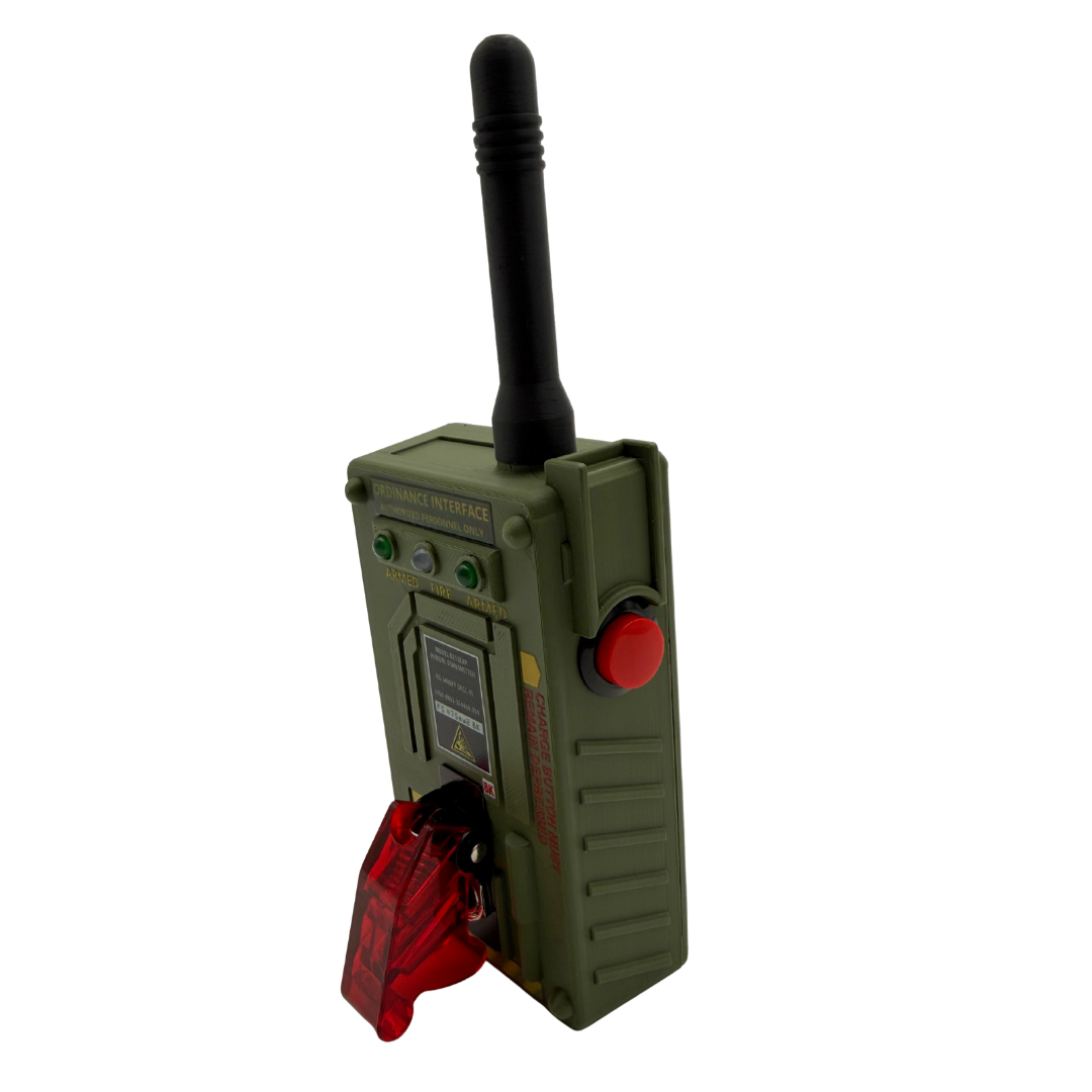 An olive green toy or model walkie-talkie with a black antenna, a red button, and a red translucent front cover, shown on a plain white background.