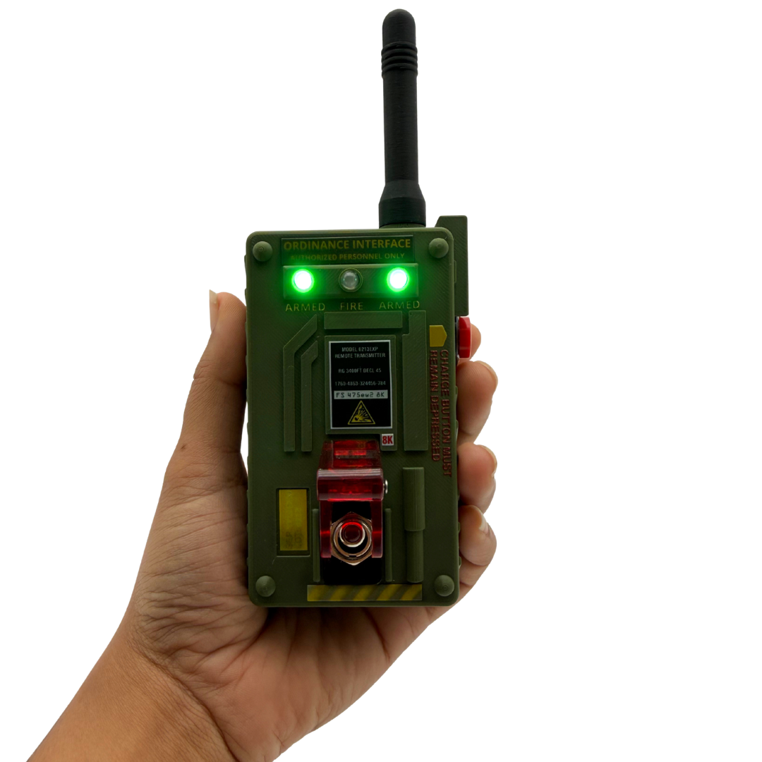 A hand holding a green military-style electronic device with a black antenna, glowing green lights, and red accents, shown against a plain white background.