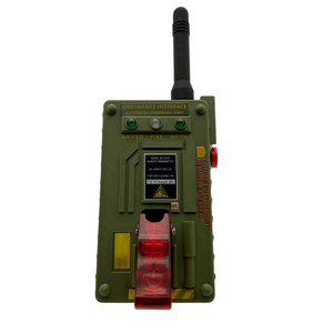A military-style ordinance device or training gun in olive green plastic, featuring a black antenna, green indicator lights, a red translucent front window, and printed text including 'ORDINANCE INTERFACE' and 'ARMED FIRE'.