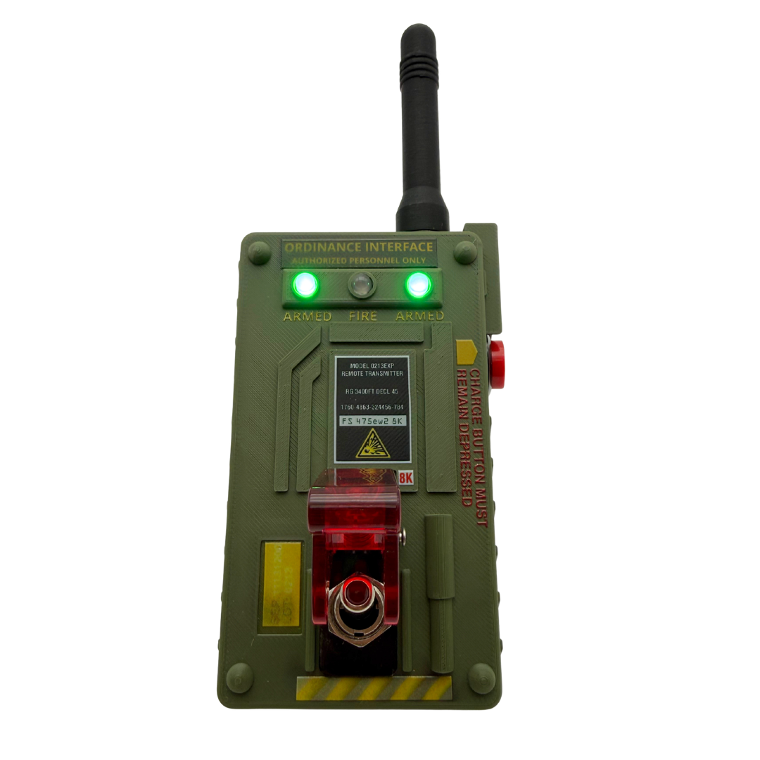 A green tactical-style electronic device with an antenna, illuminated green lights, warning labels, and red translucent front panel details, isolated on a white background.