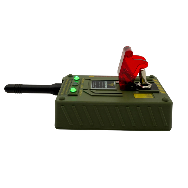A military-style electronic device with a green plastic housing, a black antenna, green indicator lights, a red translucent switch cover, and a metal lever on top, shown against a plain white background.